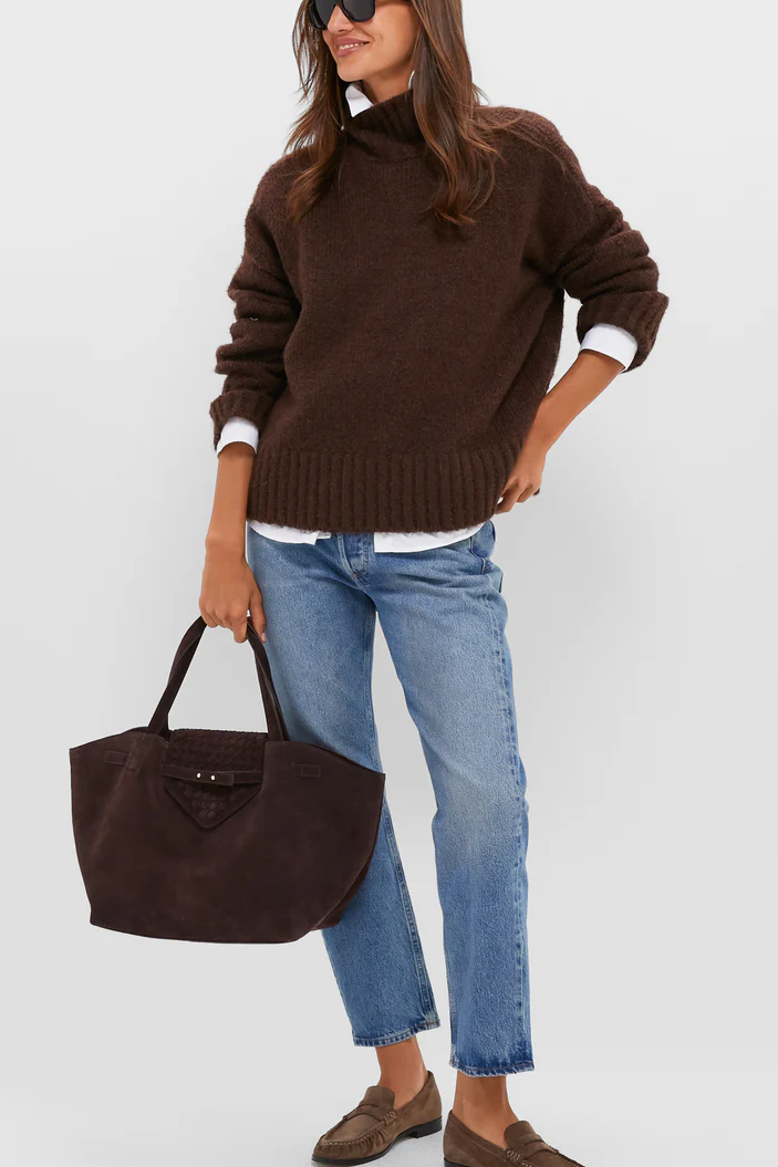 A WOMAN WEARING A SWEATER WITH JEANS AND LOAFERS AND A TOTE BAG